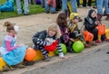 A row of children dressed in fun Halloween costumes, sit on a curb waiting for the parade for