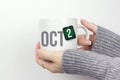 October 2nd. Day 2 of month, Calendar date. Closeup of female hands in grey sweater holding cup of tea with month and calendar