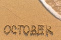 October - word drawn on the sand beach with the soft wave.