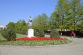Statue of a collective farmer on a pedestal. The legacy of the Soviet era. A flower bed with tulips and young trees in
