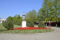 Statue of a collective farmer on a pedestal. The legacy of the Soviet era. A flower bed with tulips and young trees in