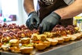 Odziena / Latvia - August 24th, 2018: Male Chef Putting Ingredients of Burgers on a Sliced Bread Spread on a Table in Black Gloves