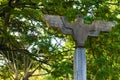 An off-centered shot of an old, bird shaped, outdoor, cement lighting post., with a wide wing span, located in a Thai public park.