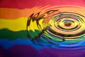 Off centre water splash and circular ripples on the surface reflecting the Gay Pride Extinction Rebellion flag and logo Royalty Free Stock Photo