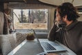Off grid job lifestyle with mature man working on laptop inside a camper van and looking the forest outside the window. Van life Royalty Free Stock Photo