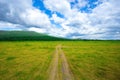 Off road way toward mountain surrounded by meadow grass field under beautiful clear blue sky. The off road way show tire trace fro Royalty Free Stock Photo