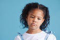 Offended little hispanic girl looking sad and upset while posing against a blue studio background. Unhappy preschooler