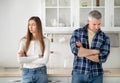 Offended mature married couple standing in kitchen with crossed arms after quarrel at home