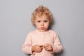 Offended sad baby girl with blonde wavy hair wearing rose shirt isolated over gray background looking at camera with blowing Royalty Free Stock Photo