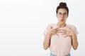 Offended and shocked female tutor in glasses and hair bun holding breath and hands on chest in insulted posture Royalty Free Stock Photo