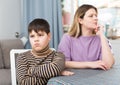 Offended son sitting at tablr after quarrel with mother at home Royalty Free Stock Photo