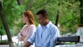 Offended teen girlfriend and boyfriend sitting separately on bench in park