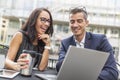 Office colleagues discuss and laugh over a laptop sitting with a coffee outdside