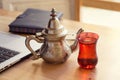 Office desk gray laptop silver arabic tea pot and notebook red cup Royalty Free Stock Photo
