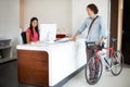 Office, desk and man with bike for business, travel and talking about commute to work with receptionist in morning Royalty Free Stock Photo