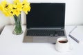 Office desk table with laptop computer with black screen, supplies, cup of coffee or tea, flowers bouquet on white table Royalty Free Stock Photo