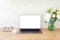 Office desk table with laptop computer with blank screen mockup and flowers bouquet, coffee cup, glasses, notepad on wooden Royalty Free Stock Photo