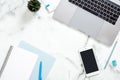 Office desk table with laptop computer, smartphone with blank screen, diary, blue stationery, succulent plant on white marble Royalty Free Stock Photo