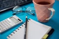 Office desk table with other supplies. Notepad with black pencil and calculator near cup of tea, glasses and keyboard of Royalty Free Stock Photo