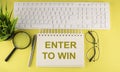 Office desk table Top view with keyboard and notebook text ENTER TO WIN on yellow background