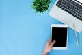 Flat lay top view mockup photo of working space with laptop and a hand holding on smart tablet on blue pastel background. Royalty Free Stock Photo