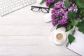 Office desktop with a bouquet of lilacs, coffee cup, keyboard, notebook and pen on white boards