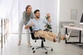 Office employee giving her colleague ride in chair at workplace