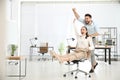 Office employee giving his colleague ride in chair at workplace. Space for text