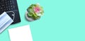 Office flat lay with laptop, empty notepad and medicine mask on mint background. Royalty Free Stock Photo