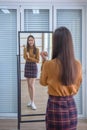 An office girl wearing a short plaid skirt stands looking at her reflection in the mirror Royalty Free Stock Photo