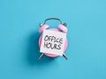 Office hour concept in business or education. Pink alarm clock with a note paper on blue background with the word office hours