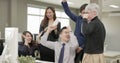 Office male in glasses hears good news on computer and rejoices with colleagues hugging and waving their hands