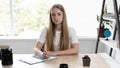 Office manager blonde girl sitting in the office by the window at the desk works making notes in a notebook. Bright room