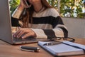 Office Portable work area. Outdoor office with trees. Young girl talking on the phone and working with laptop Mobile phone glasses