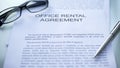 Office rental agreement lying on table, pen and eyeglasses on official document