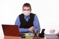 Office specialist in a protective medical mask sits at a desk and looks into the frame