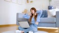 Asian young woman working on laptop while seated on floor next to couch at home Royalty Free Stock Photo