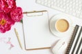 Office table with computer, empty clipboard, cup of coffee and peony flowers.