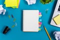 Office table desk with set of colorful supplies, white blank note pad, cup, pen, pc, crumpled paper, flower on blue Royalty Free Stock Photo