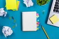 Office table desk with set of colorful supplies, white blank note pad, cup, pen, pc, crumpled paper, flower on blue Royalty Free Stock Photo