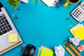 Office table desk with set of colorful supplies, white blank note pad, cup, pen, pc, crumpled paper, flower on blue Royalty Free Stock Photo