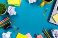 Office table desk with set of colorful supplies, white blank note pad, cup, pen, pc, crumpled paper, flower on blue Royalty Free Stock Photo