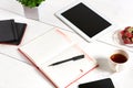 Office table desk with set of supplies, white blank notepad, cup, pen, tablet, flower on white background. Top view