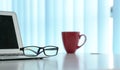 Office table with notebook laptop, eading glasses and coffee mug. Copy space