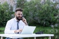 Office worker guy at desk using desktop computer laptop and phone at work, smiling, looking at screen. Outdoor Royalty Free Stock Photo