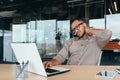 Office worker has severe neck pain, businessman in glasses working inside office using laptop at work, african american Royalty Free Stock Photo