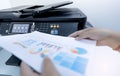 Office worker prints paper on multifunction laser printer. Copy, print, scan, and fax machine in office. Document and paper work.