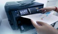 Office worker prints paper on multifunction laser printer. Copy, print, scan, and fax machine in office. Document and paper work.