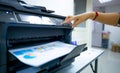 Office worker prints paper on multifunction laser printer. Copy, print, scan, and fax machine in office. Document and paper work.