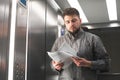 Office worker in a shirt standing in an elevator holds documents and reads in his hands. Business man is studying paper in the Royalty Free Stock Photo